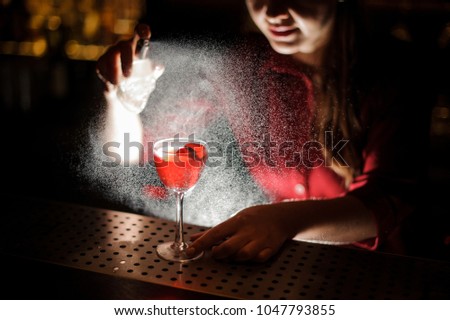 Woman bartender sprinkling a cocktail glass filled with tasty Aperol syringe summer cocktail with a peated whisky on the bar counter