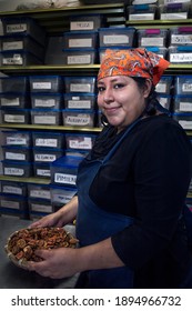 Woman With A Basket Of Dehydrated Guava. At The Background A Rack With Plants