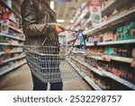 Woman, basket and hands of customer in grocery store, goods discount and shelves for deal. Female person, sale and shop for options on offer, retail purchase and browsing supermarket shelf in aisle