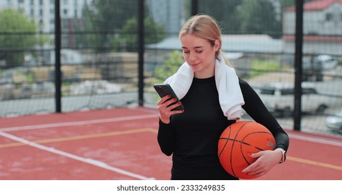 Woman with basketball ball and smartphone on basketball court. Using smartphone after training. Concept of sport, active lifestyle. - Powered by Shutterstock