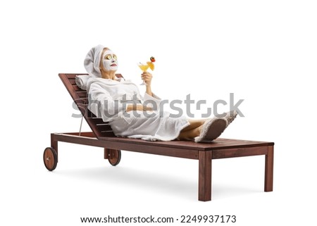 Woman in a bathrobe laying with a face mask and cucumbers on eyes and holding a glass of cocktail isolated on white background