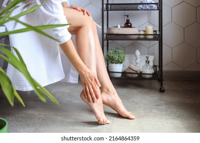 a woman in a bathrobe touches the skin of her legs, applying lotion, doing body and skin care in the bathroom. Spa, laser epilation, depilation. Close-up