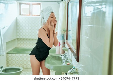 Woman in bathroom applies moisturizer for skincare routine. Gentle touch on soft skin, enjoys beauty ritual with cream. Focus on home self-care, represents wellness industry trends in personal care. - Powered by Shutterstock