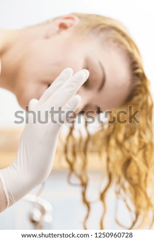 Woman in bathroom putting on white latex protective gloves before hair dyeing.