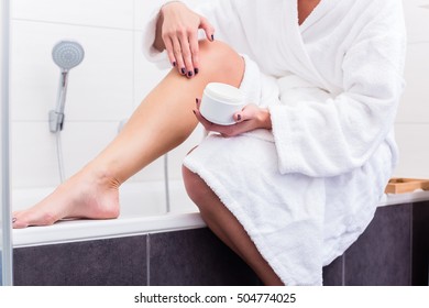 Woman In Bathroom Sitting At Edge Of Bathtub Putting On Lotion On Legs