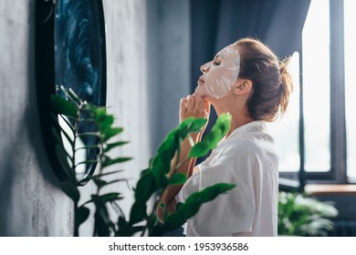 Woman In The Bathroom Taking Care Of Her Facial Skin By Applying A Mask To Her Face