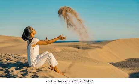 woman at the beach of Maspalomas Gran Canaria Spain, a girl at the sand dunes desert of Maspalomas Spain Europe throwing sand in the air
