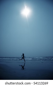 Woman At The Beach Running To The Water In The Deep Dark Night. Blue Color Toning Added For Coolness Of The Night