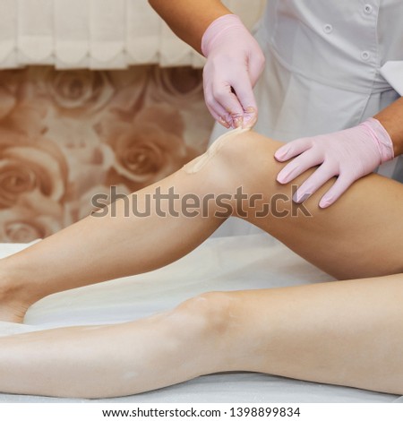 woman beautician conducts a procedure of sugar depilation with honey on the legs of a lying girl in a professional salon for health and skin care. Modern way of hair removal