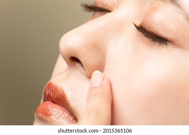 A woman with beautiful skin is pointing at her nose.
