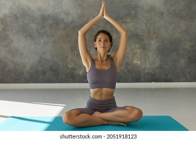 Woman With Beautiful Slim Fitness Body Wearing Crop Top And Bike Sport Shorts Sitting In Lotus Posture Putting Hands Folded In Praying Position Up, Inhaling Deeply Looking Concentrated And Thoughtful