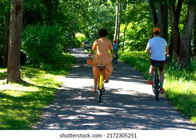 A Woman In A Beautiful Yellow Dress With Shoes And A Small Matching Handbag And A Man In Bright Clothes On A Bike Ride. Repino, St. Petersburg, 25.06.2022
