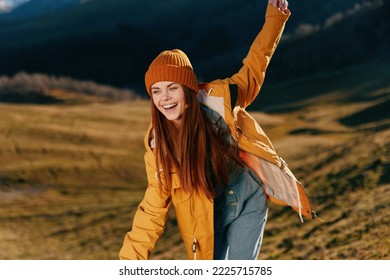 Woman beautifully running up the hill to the camera smile with teeth in the mountains in the autumn in a yellow raincoat and jeans happy sunset trip on a hike mountains in the snow, freedom lifestyle - Shutterstock ID 2225715785