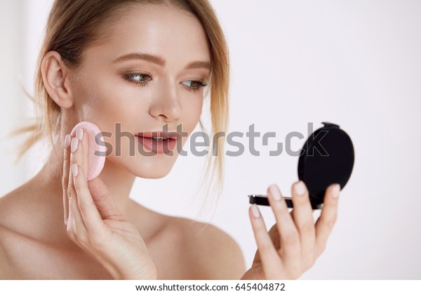 「女性の美顔。化粧粉の基礎を施したクッションパフと鏡で美しい女性の接写。肌が柔らかく、化粧品の生気のないセクシーな女の子のポートレート。高解像