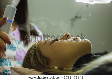 A woman in a beauty parlor.  Eyelash extension procedure - Master applies steam with an electronic device.  Concept of beauty and care.