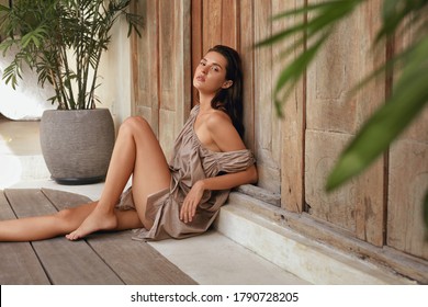 Frauenporträt Beauty. Schönes Modell mit perfektem Körper, das sich in der Nähe von Holzwänden auf der Terrasse befindet. Brunette in verführerischer Kleidung auf dem Boden und Blick auf Kamera. 
