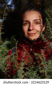 Woman Beauty Portrait With Foreground Of Juniper. Female Model Outdoor Portrait. Girl In Red Coat Posing In Autumn Nature