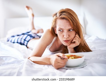 Woman In Bed Eating Chicken Noodle Soup While Sick