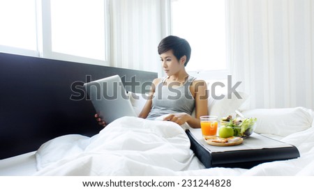 Woman in bed with laptop and breakfast
