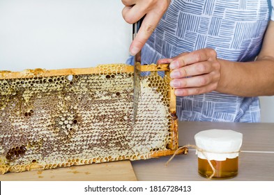 woman beekeeper, female chef cuting for knife a honeycomb frame to filling glass jar with natural flower honey. copy space, place for text