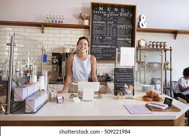 Woman behind the counter of a coffee shop looking to camera