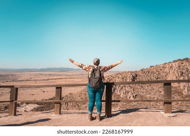 woman from behind enjoying her trip raising her hands observing the landscape