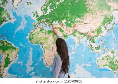 Woman from behind pointing on world map, geography