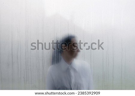 Woman behind wet foggy window. Loneliness concept
