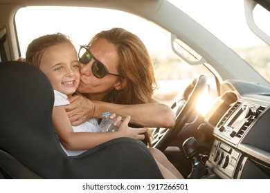 Woman behind the wheel with white t-shirt in holiday context kisses her daughter with smiling expressions