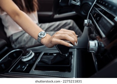 A woman behind the wheel. A young woman's hand on the gear selector in a modern car. Automatic transmission gear shift. - Shutterstock ID 2275211831