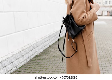 Woman In Beige Coat Holding Black Backpack. Trendy Stylish Casual Outfit. Details Of Everyday Autumn, Winter Or Spring Look. Street Fashion.