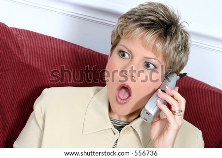 Woman in beige suit speaking on cordless phone.  Shocked expression. Blonde hair, green eyes.
