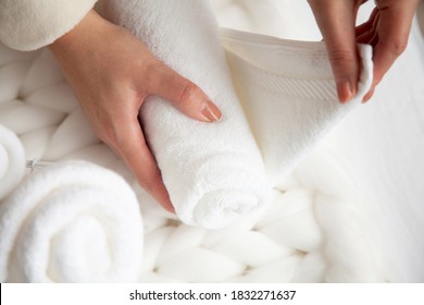 Woman In Beige Warm Robe Is Folding The Clean White Hand Towels And Putting Into A Metal Mesh Basket On Black Background. Copy Space On Black Background. Cleanliness And Organisation Concept.