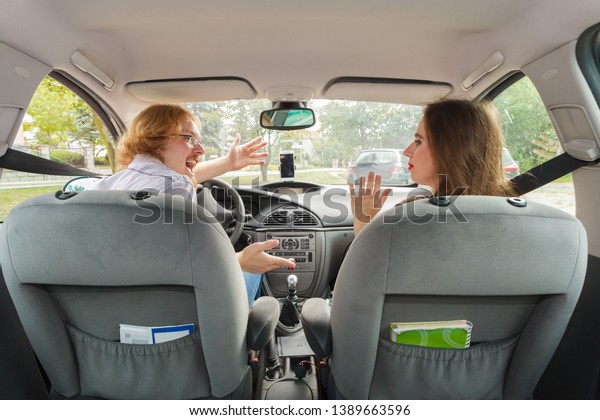 Woman being not impressed by her boyfriend
driving skills. Displeased female looking at happy fooling around
man behind steering wheel inside
car.