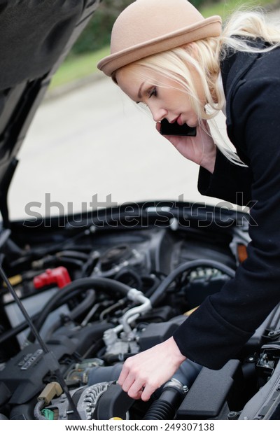 Woman\
being talked through roadside assistance on her broken down car on\
her mobile phone as she tinkers with the\
engine