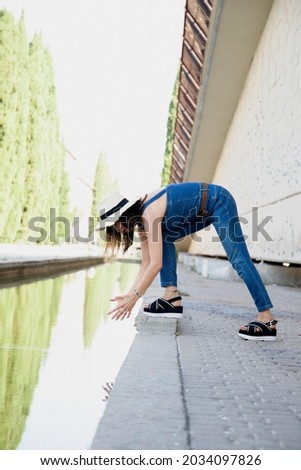 woman bending over to get water from the pond