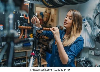 Woman bicycle mechanic is repairing a bike in the workshop. Technician woman fixing bicycle in repair shop. Young woman adjusting bike chain and repairing bicycle. Bike service.  - Powered by Shutterstock