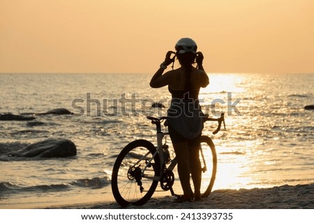 Woman with bicycle on the beach in sunrise.