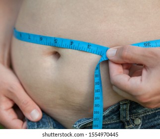 Woman With Big Belly. Jeans That Don't Fit Any More. Measuring The Waist With Tape Measure.