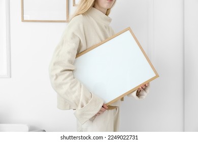 Woman with big blank frame near light wall