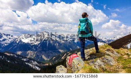 A woman with big hiking backpack hiking to Himmeleck peak, Austria. There is a massive mountain range in the back, partially covered with snow. Early spring vibes. Freedom and adventure.