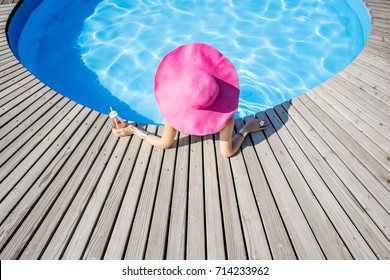 Woman In Big Pink Sunhat With Cocktail Drink Relaxing At The Round Swimming Pool With Blue Water Outdoors. Top View