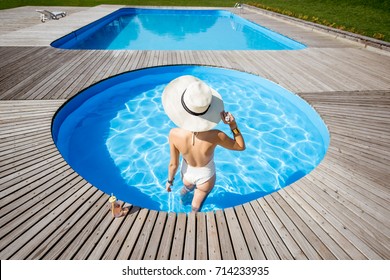 Woman In Big Sunhat With Cocktail Drink Relaxing At The Round Swimming Pool With Blue Water Outdoors. Top View