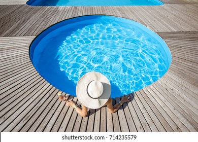 Woman In Big Sunhat With Cocktail Drink Relaxing At The Round Swimming Pool With Blue Water Outdoors. Top View