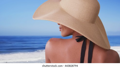 Woman with big sunhat looking out over ocean on vacation