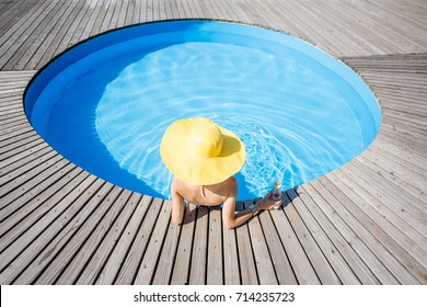 Woman In Big Yellow Sunhat With Cocktail Drink Relaxing At The Round Swimming Pool With Blue Water Outdoors. Top View