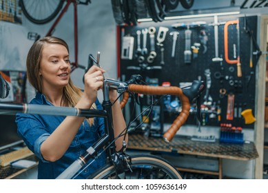 Woman bike mechanic working on bicycle. Young woman master is fixing wheel of city-bike in bicycle service. Technical expertise taking care Bicycle Shop - Powered by Shutterstock