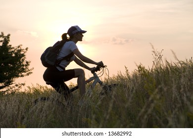 woman biker on a meadow in sunset