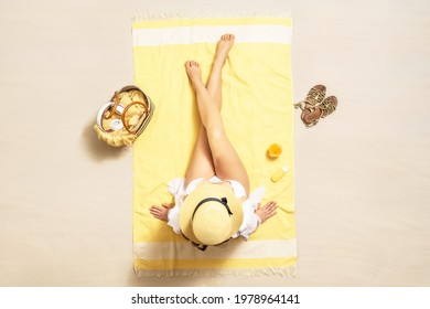 Woman in bikini applying sunscreen on skin sitting and sunbathing on the towel. Female relaxation on the sand beach at summer vacation. Top, aerial view. 