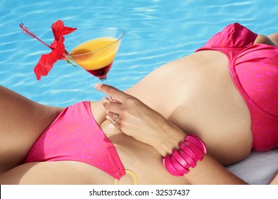 Woman in a bikini with a cocktail by a blue swimming pool